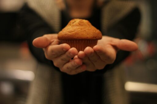 A person holding a freshly baked muffin with both hands extended